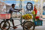A flower vendor pushes his cart past a mural of Ernesto "Che" Guevara reading “Until victory, always” in Havana on Feb. 25, 2026, as Cuba’s US-imposed oil blockade forces workers to change jobs and abandon cars amid blackouts and fuel shortages.