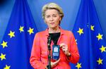 A person standing in front of European Union flags holds up a smart phone to display a digital COVID-19 travel certificate on the screen.