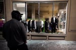 In this Nov. 4, 2020, file photo, a man stands in front of a broken display window at a retail store during protests in Portland.