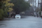 This photo shows a street in Charleston, South Carolina, that has been flooded by rain from Hurricane Ian in 2022. Water covers the street and rises up to the front fender of a vehicle parked on the side of the street. The poles of parking meters are partially submerged in the water.