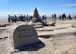 A block of sand in the foreground reads "TURTLES ALL THE WAY DOWN." A large turtle has a smaller turtle on its back which has a castle on its back. Spectators look on in the background.