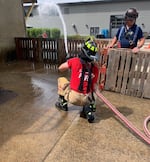 A firefighter sprays water from a firehose as another looks on.