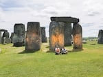 In this handout photo, Just Stop Oil protesters sit after spraying an orange substance on Stonehenge, in Salisbury, England, on Wednesday. (Just Stop Oil via AP)