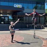 Achillea Grim, left, and Harlequin Grim, right, perform juggling with a 7-foot-tall unicycle at OPB headquarters in Portland, Ore., on July, 15, 2024.