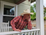 A man with a cowboy hat leans over a fence, resting his chin on his hand.