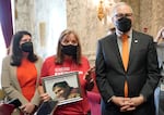 FILE: Kim Gatbunton, center, holds a photo of her son Josh Gatbunton, who was shot and killed during a 2008 robbery at an apartment in Tacoma, Wash., as she talks with reporters along with Washington Gov. Jay Inslee, right, Wednesday, March 23, 2022, at the Capitol in Olympia, Wash., after Inslee signed a package of bills to tighten gun laws in Washington state. Those laws go into effect July 1, 2022.