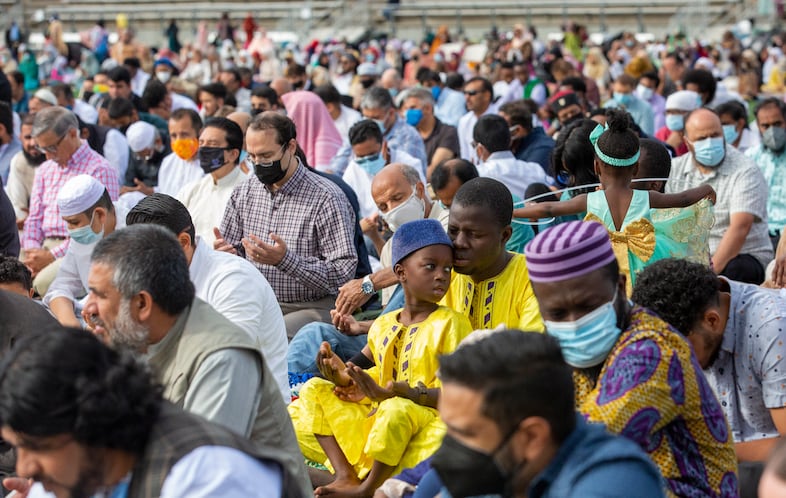 Muslim community members gather at Hillsboro stadium in Portland, Oregon for a prayer and festivities celebrating Eid Al-Adha. They raise their hands to pray at the end of the sermon before celebrations begin.