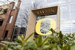 A glass-walled academic building has a large yellow University of Oregon "O" emblem emblazoned on its exterior.