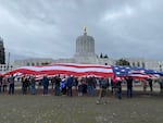 Protesters in Salem on Jan. 1, 2021, stand together underneath a giant U.S. flag in front of the Oregon Capitol building.