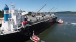 Two tug boats approach a cargo ship in a body of water