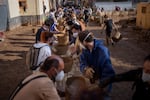 Volunteers make a human chain to evacuate the mud in buckets in an area still flooded with mud in Masanasa, Valencia, Spain, Thursday, Nov. 7, 2024.