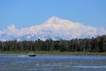 Denali, the tallest mountain on the North American continent, looma behind a boat on the Susitna River near Talkeetna, Alaska, in June 2021.