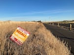 A sign that states "Vote yes, recall Jim Doherty And Melissa Lindsay" is posted in some sage brush on the side of the road. The sign includes an illustrated ambulance  in its bottom left-hand corner.