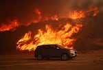 A vehicle rides past a hillside engulfed in flames caused by the Hughes Fire in Castaic, Calif., Wednesday, Jan. 22, 2025.