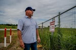 A man wearing a baseball cap stares into a lot with tall grass and a fence that says "no trespassing."