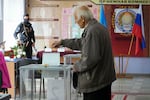 A man casts his ballot as a Russian soldier looks on in Luhansk, Ukraine, on Tuesday. Voting began Friday in four Moscow-held regions of Ukraine on referendums to become part of Russia.