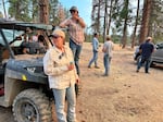 Two women standing on a side-by-side all-terrain vehicle. Other people in the background standing and talking.