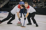 Two men in Team USA shirts and black pants are on an ice rink with curling sticks mid competition.