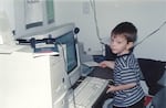 A child sits at a large 1980s desktop computer.