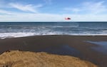 In this photo provided by the Oregon State Police from 2017, a U.S. Coast Guard helicopter searches a beach about two miles north of Cape Blanco, Ore., searching for a pair of men swept out to sea.