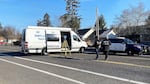 A Portland Police Major Crash Team van with sliding door open is parked across a road, next to a blue and white Portland Police SUV. Two officers stand in the road next to the vehicles, with yellow tripod measuring device.