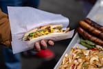A customer holds a bacon-wrapped hot dog from a vendor at Fisherman’s Wharf in San Francisco on April 24, 2025. Portland City Councilor Mitch Green introduced a proposal to remove bureaucratic barriers for street vendors.