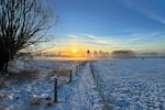 The sun rises over a snow-covered landscape in Denderhoutem, Belgium.