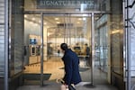 In this photo, a man walks past a branch of Signature Bank in New York City on March 13, 2023. The bank has double glass doors, and the name "SIGNATURE BANK" appears in capital letters above the doors.