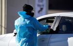 FILE - A medical technician performs a nasal swab test on a motorist queued up in a line at a COVID-19 testing site near All City Stadium Dec. 30, 2021, in southeast Denver. Millions of workers whose jobs don’t provide paid sick days are having to choose between their health and their paycheck as the omicron variant of COVID-19 rages across the nation. While many companies instituted more robust sick leave policies at the beginning of the pandemic, those have since been scaled back with the rollout of the vaccines, even though the omicron variant has managed to evade them.