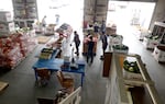 Farmers market workers help customers as they browse watermelons and other produce in a large warehouse-like setting.