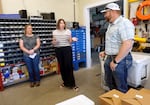 McDonald, in a beige striped blouse and a long black skirt talks and gestures at Willman, in a short sleeved Western shirt and blue jeans as they stand in a well-stocked toolshed.