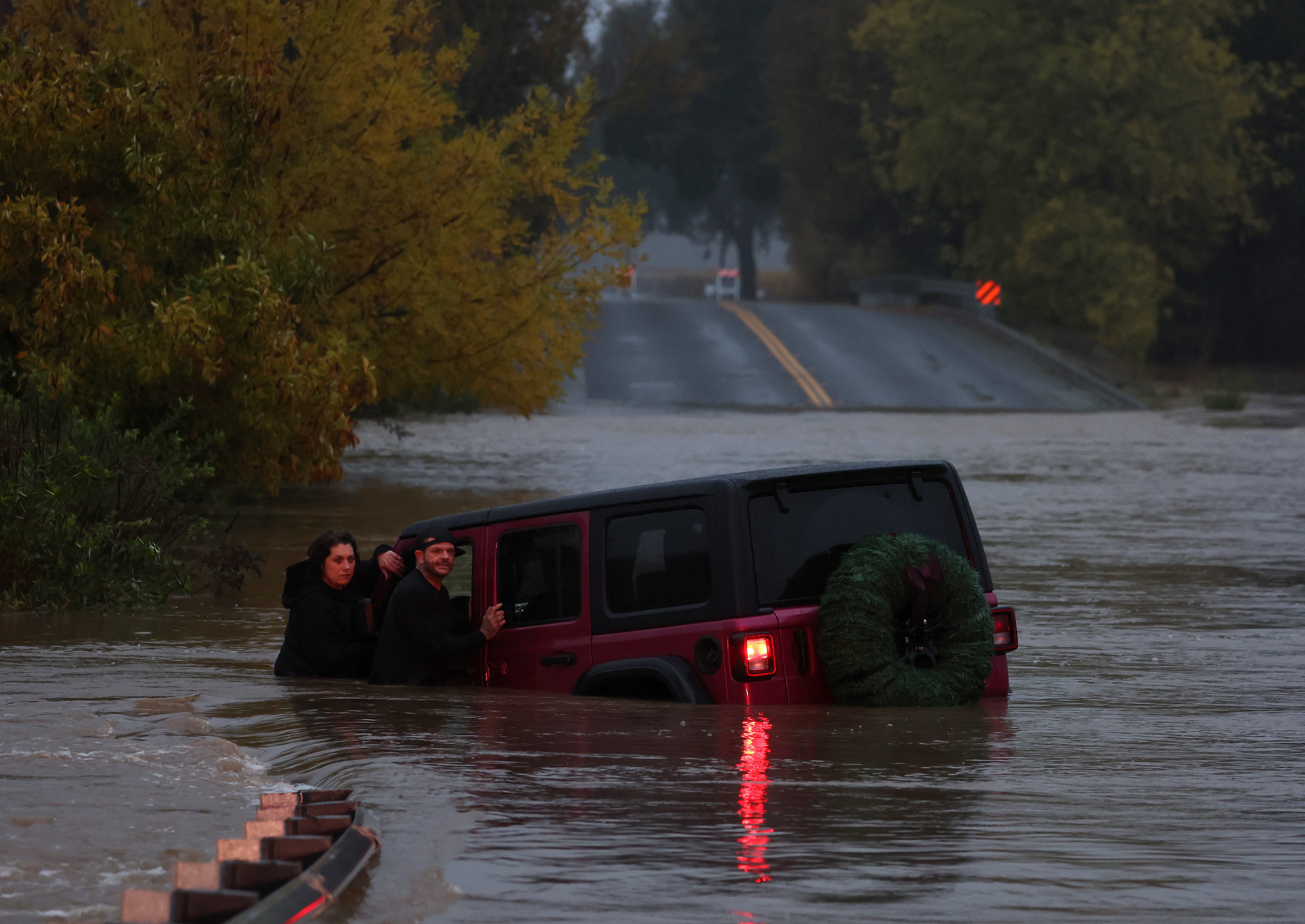 A couple waits for a rescue crew after their car got stuck in deep floodwaters in Windsor, Calif., in November 2024. Experts say you should break your window and climb out as quickly as possible.