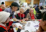 Michiko Usui Kornhauser, center, smiles as volunteer Tracy Yotsuuye, left, serves her a meal during an Ikoi no Kai lunch, in Portland, Ore., Dec. 16, 2024. Kornhauser usually comes to these lunches every day they are offered and says the social connection is good for her health.