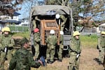 In this photo provided by the Japan Self-Defense Forces Akita Camp, Self-Defense forces personnel unload a bear cage from a military truck in JSDF Akita Camp, Akita, northern Japan, Thursday, Oct. 30, 2025.