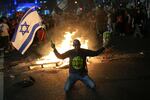 A protester holds an Israeli flag as Israelis light a bonfire during a protest after Prime Minister Benjamin Netanyahu has dismissed his defense minister Yoav Gallant in a surprise announcement in Tel Aviv, Israel, Tuesday, Nov. 5, 2024.