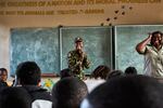 Black Mamba anti-poaching unit member Nkateko (left) and Bush Babies education officer Lewyn (right) laugh after realising that three of the students in their class are the children of fellow Black Mambas, Maseke Primary School, South Africa, 2017. 

The Black Mambas are an all-female unit made up of local women who wanted to help protect the natural heritage of South Africa. Their approach is radically different to that of traditional anti-poaching efforts which rely on the threat of force and extreme violence. The main tools in the Mambas’ arsenal are empathy and kindness, rather than the guns and helicopters employed by rangers. At Balule Nature Reserve, the latter are only used in extreme situations. 

The Mambas prefer to use visual policing – daily foot patrols through the reserve  – to check on the local landscape and the animals that live here, and to build an intimate relationship with the local environment. They know every tree in the reserve, they care for and release the trapped and injured animals they find, and watch out for each other as they check the endless fence line that surrounds Balule.  

Nkateko and her fellow Mambas use the fact that they live in the same villages as many of the poachers do, to engage with and confront them as mothers, sisters or friends rather than as soldiers or rangers. They visit schools to teach children about the importance of wildlife conservation. And, they serve as role models in their own communities – aware that food insecurity is a significant driver for poachers, Nkateko started a feeding program in her own village. 

By creating an environmentally literate community which appreciates the value of keeping animals alive in their natural habitats, the Mambas want to make sure that South Africa’s wildlife will be around long enough for their own children to appreciate. 