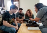 Class of 2025 student Jason, left, with his parents Jay and Tara at home in Woodland, Washington in Sept. 2024, as OPB reporter Elizabeth Miller, right, shows them something on her phone.