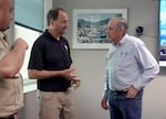 A man speaks to another man in an office room.