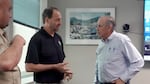 A man speaks to another man in an office room.