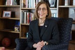 Kate Brown wears a suit and sits in an armchair in front of a wooden bookcase.