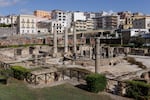 Ancient Roman ruins are seen surrounded by modern buildings.