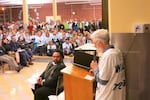 Business owner Mike Roach wears a white T-shirt in support of Rieke Elementary School. Just past the lectern sits Jason Trombley, the chair of Portland's District-wide Boundary Review Advisory Commitee. In the background, parents in light blue shirts represent Bridlemile Elementary. 