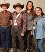 Four people pose for a photo. The two men on the left wear cowboy hats.