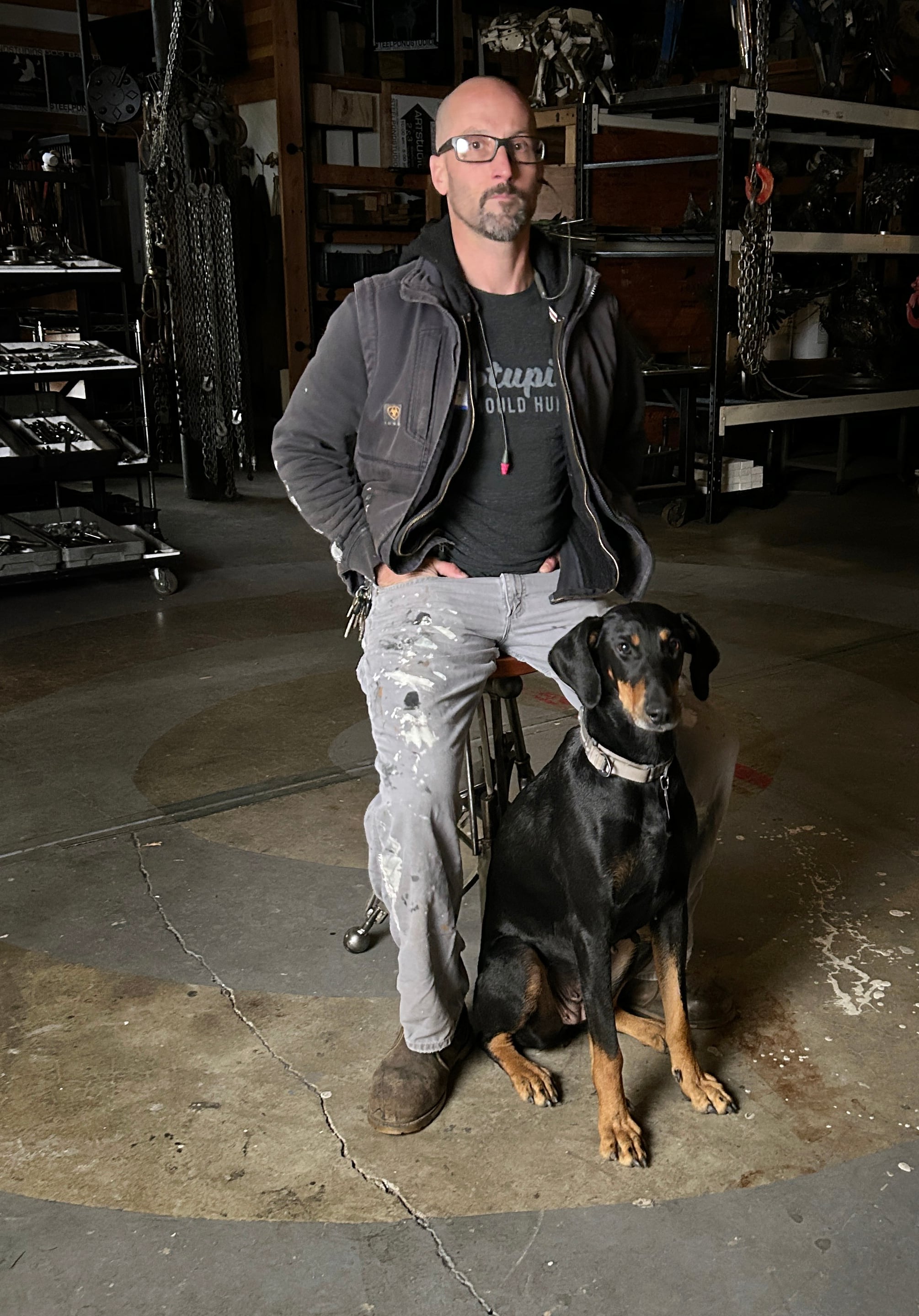 Travis Pond sits with his dog Nola. Pond works out of his Oregon City studio, where he takes pieces of scrap metal and repurposes them into intricate sculpted works.
