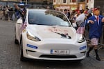 A reveler disguised as President Trump walks next to a car bearing a picture of Elon Musk's salute during the yearly carnival parade in the streets of Aalst, Belgium on March 2, 2025.