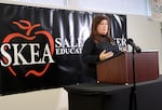 Salem-Keizer teacher union president Tyler Scialo-Lakeberg speaks at a lecture with a microphone. There is a union poster behind her on the wall.
