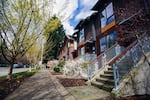 This photo of the Bryant Heights development in Seattle shows a row of town houses with a sidewalk in front of them. Trees rise up from the strip of grass between the sidewalk and the road.