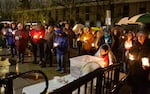 A crowd stands in the rain holding candles.