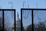 The dome of the US Capitol building in Washington, D.C., is visible through a barbed-wire topped metal fence.