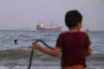 Children play in the water along the shore as a mix of bulk carriers, cargo ships, and service vessels sit offshore in the Strait of Hormuz off Bandar Abbas, Iran, Sunday, April 26, 2026.
